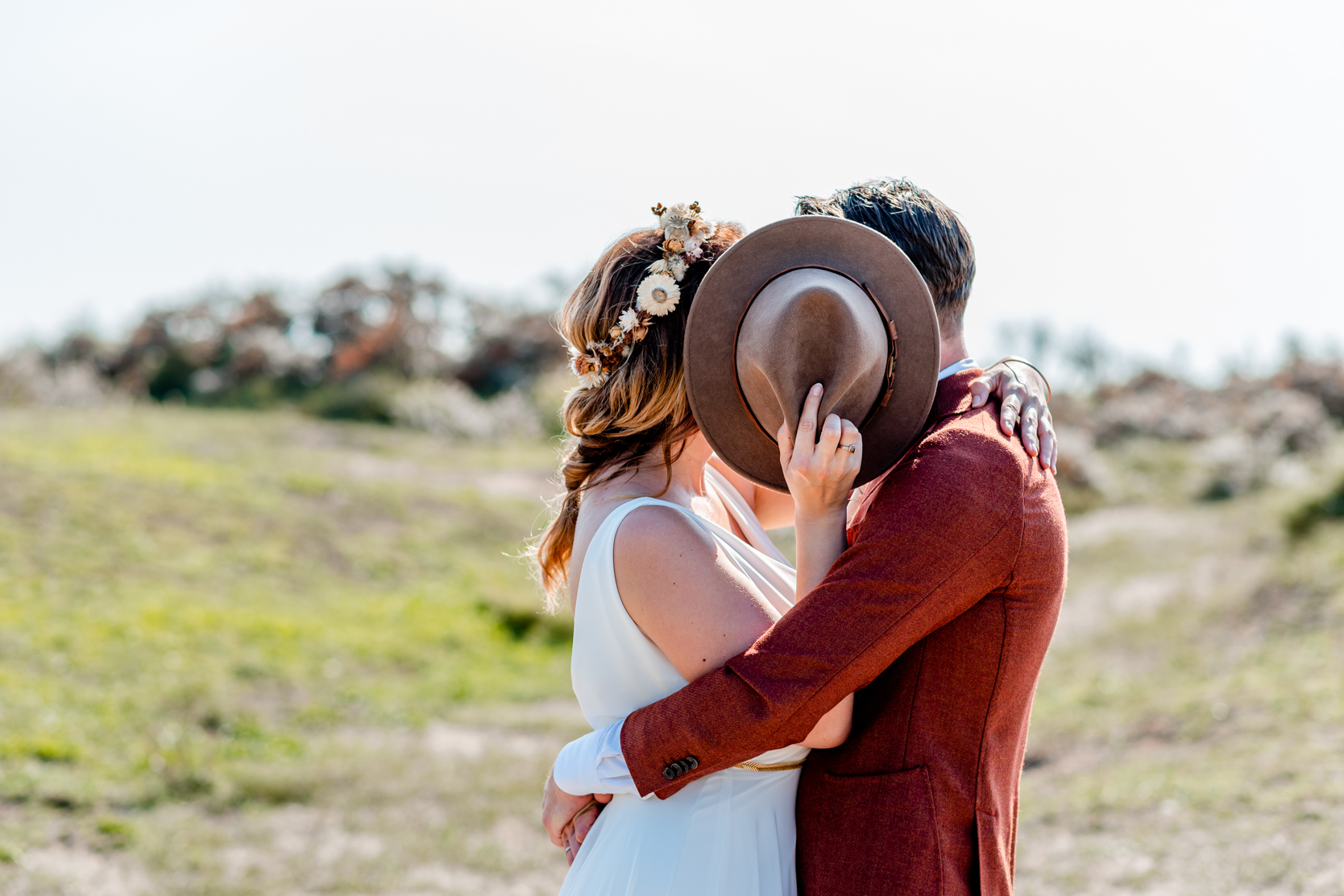 Bruidspaar verstopt achter hoed strand bruiloft