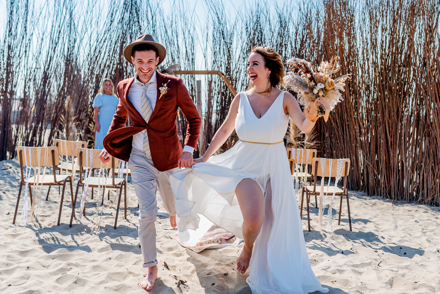 Bruidspaar rent lachend weg van de ceremonie op het strand
